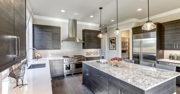 Modern gray kitchen features dark gray flat front cabinets paired with white quartz countertops and a glossy gray linear tile backsplash. Bar style kitchen island with granite counter. Northwest, USA