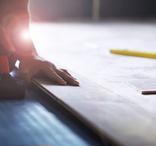 Installing laminated floor, detail on man hands holding wooden tile, over white foam base layer, small pile with more tiles background