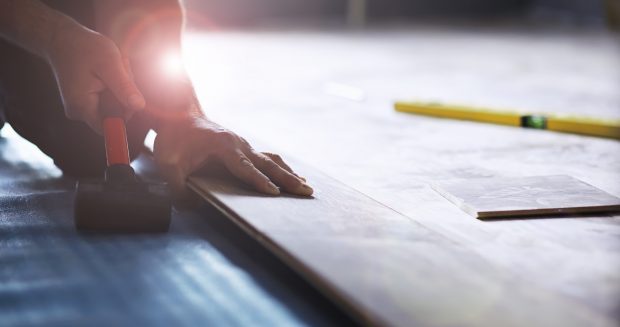 Installing laminated floor, detail on man hands holding wooden tile, over white foam base layer, small pile with more tiles background